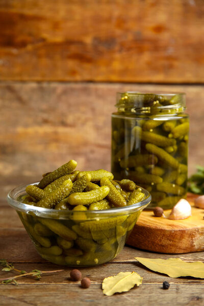 Glass bowl with tasty pickled cucumbers and different spices on wooden background