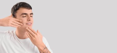 Gri arkaplan üzerinde yüz geliştirme egzersizi yapan genç bir adam.