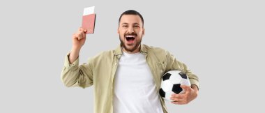 Pasaportu, biletleri ve arka planda futbol topu olan mutlu bir erkek taraftar.