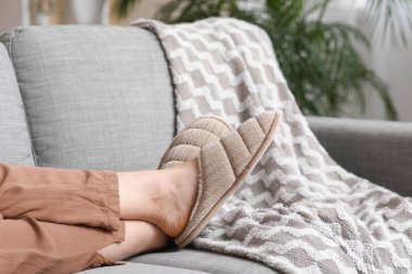 Oturma odasındaki kanepede rahat terlikler içinde kadın bacakları.