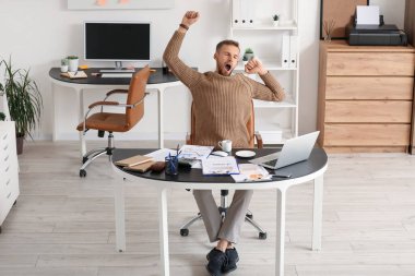 İş yerinde gözlüklü genç bir işadamı, ofiste belgeler ve bilgisayarla dinleniyor.