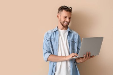 Gözlüklü genç işadamı bej arka planda dizüstü bilgisayar kullanıyor