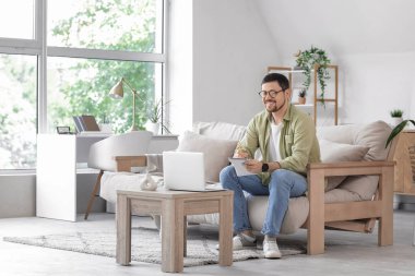 Dizüstü bilgisayarı ve not defteri olan genç erkek öğretmen evde online ders veriyor.