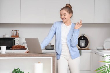 Genç kadın mutfaktaki masada modern dizüstü bilgisayar kullanıyor.