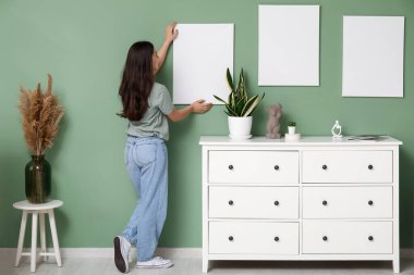 Evdeki yeşil duvara boş tuval asan genç bir kadın. Arka plan