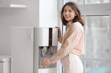 Güzel genç bir kadın mutfaktaki soğutucudan cama su dolduruyor.