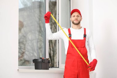 Oda penceresinin yanında mezurası olan bir erkek işçi.