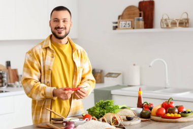 Genç adam mutfakta lezzetli Meksika tacoları hazırlıyor.