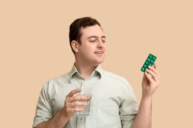 Haplardan su toplayan ve bej arka planda bir bardak suyu olan mutlu genç adam.