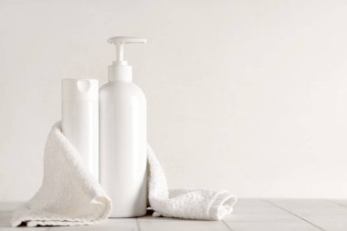 Beyaz duvarın yanındaki beyaz fayans masasının üzerinde duş jeli ve havlu şişeleriyle kompozisyon, yakın plan.