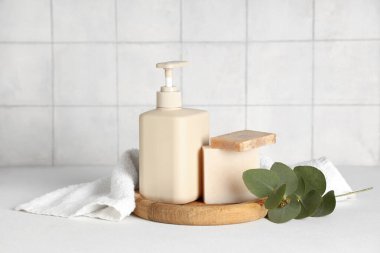 Duş jeli, sabun çubuğu ve havluyla bej fayans duvarının yanındaki masada kompozisyon