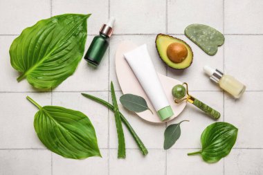 Alçı podyumlu kompozisyon, yüz masajı aletleri, beyaz karo arka planda kozmetik ürünleri ve malzemeler.