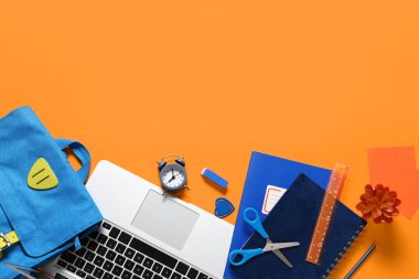 Modern dizüstü bilgisayarlı kompozisyon ve turuncu arka planda okul malzemeleri.