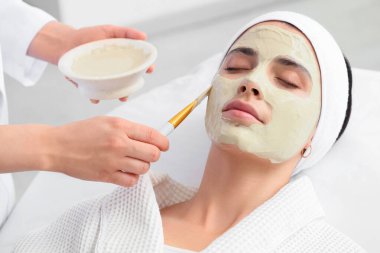 Güzellik uzmanı, kuaförde müşterinin yüzüne maske takıyor.