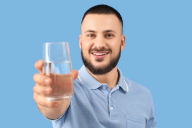 Mavi arka planda bir bardak suyu olan genç adam, yakın plan.