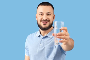 Mavi arka planda bir bardak suyu olan genç adam, yakın plan.