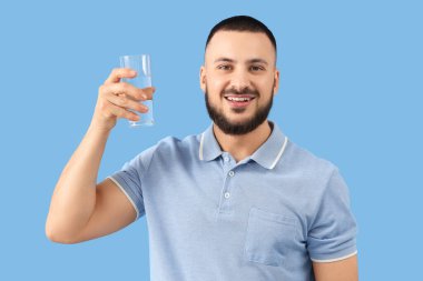 Mavi arka planda bir bardak suyu olan genç bir adam.