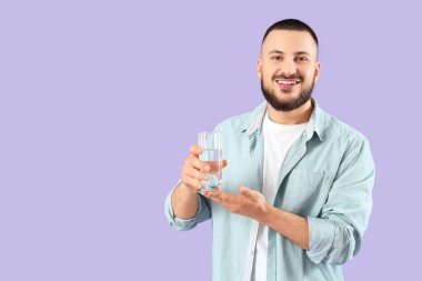 Leylak arka planında bir bardak suyu olan genç bir adam.