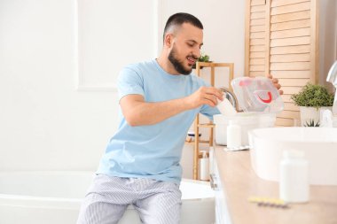 Genç adam banyoda ilk yardım çantasından hap alıyor.