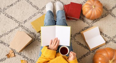 Kahveli ve balkabaklı bir kadın halıda kitap okuyor.