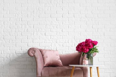 Kahve masasında mum ve beyaz tuğla duvarın yanında kanepe olan kırmızı şakayık vazosu.