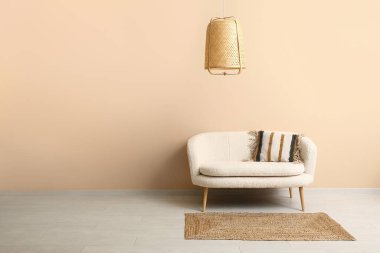 Turuncu duvarın yanında rahat beyaz kanepe, halı ve hasır lamba.
