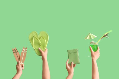 Yeşil arka planda plaj aksesuarları, pasaport ve kokteyli olan birçok el.