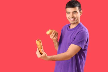 Kırmızı arka planda lezzetli sosisli sandviçleri olan mutlu genç adam.