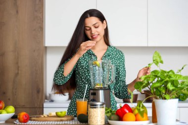 Genç bir kadın mutfakta blender ile smoothie yapıyor.