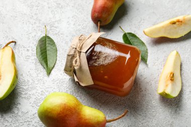 Cam kavanoz armut reçeli ve gri arka planda yapraklar.