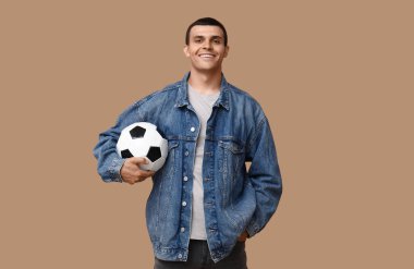 Kahverengi arka planda futbol topu olan yakışıklı bir genç.