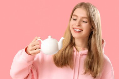 Pembe arka planda çaydanlığı olan genç ve güzel bir kadın. Yakın plan.