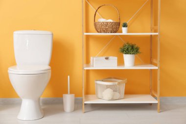 Ev bitkisi, seramik klozet ve turuncu duvarın yanında fırça bulunan şık bir banyo.