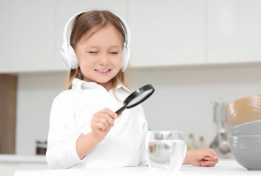 Kulaklıklı şirin küçük kız mutfakta bir bardak su büyütüyor.