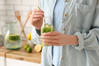 Genç bir kadın mutfakta salatalık ve nane ile doldurulmuş su şişesi tutuyor.