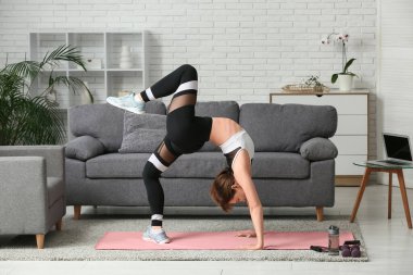 Güzel genç bir kadın oturma odasında yoga yapıyor.