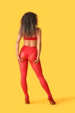 Sarı arka planda, şık kırmızı taytlı, Afro-Amerikalı genç bir kadın.