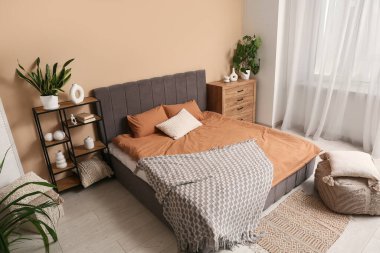 Yastıklı rahat yatak, raf ünitesi, çekmeceler ve şık yatak odasının içinde yastıklı puf.