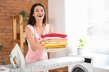 Güzel, genç, mutlu bir kadın. Banyoda bir yığın elbisesi ve ütüsü var.