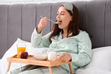 Genç ve güzel bir kadın sabah kahvaltısını yatakta yiyor.