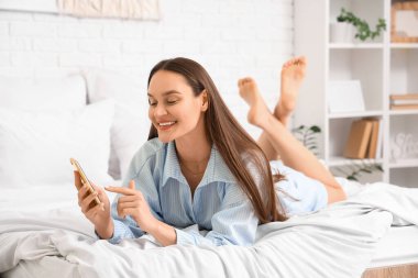 Yatak odasında cep telefonu kullanan genç kadın