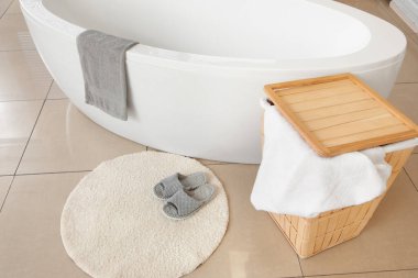 Modern banyo küvetinin yanında halının üzerinde yumuşak terlikler.