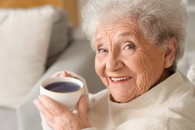 Oturma odasında bir fincan kelebek çiçeği çayıyla kıdemli bir kadın.