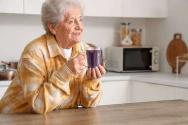 Mutfakta cam bardak kelebek çiçeği çayıyla mutlu bir son sınıf kadını.