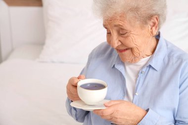 Yatak odasında bir fincan kelebek çiçekli çaylı son sınıf kadını.