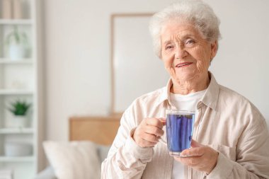Oturma odasında elinde bir bardak kelebek çiçeği çayıyla son sınıf öğrencisi.