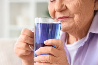 Oturma odasında cam bardak bezelye çiçeği çayıyla kıdemli kadın, yakın plan.