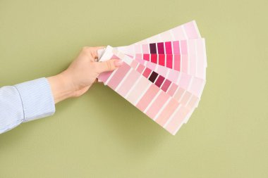 Yeşil arka planda pembe renk paletleri olan kadın eli