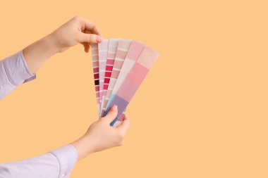 Turuncu arka planda pembe renk paletleri olan kadın elleri