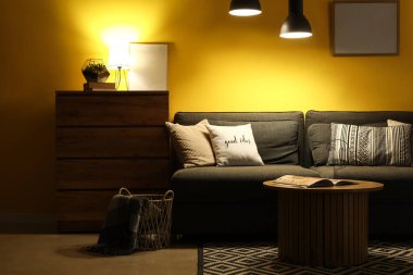 Karanlık oturma odasının içinde siyah kanepe, masa ve parlayan lambalar.